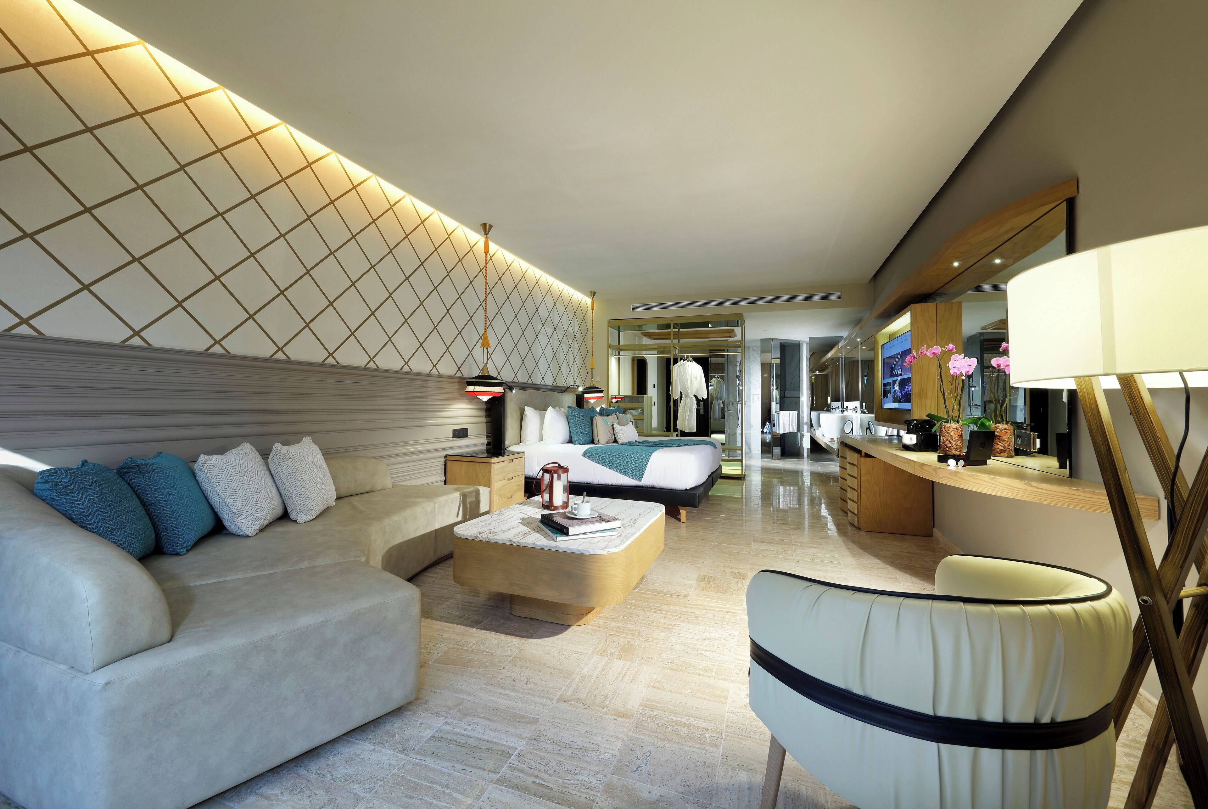 A modern hotel room with a large bed, a sofa, a coffee table, and a desk area.