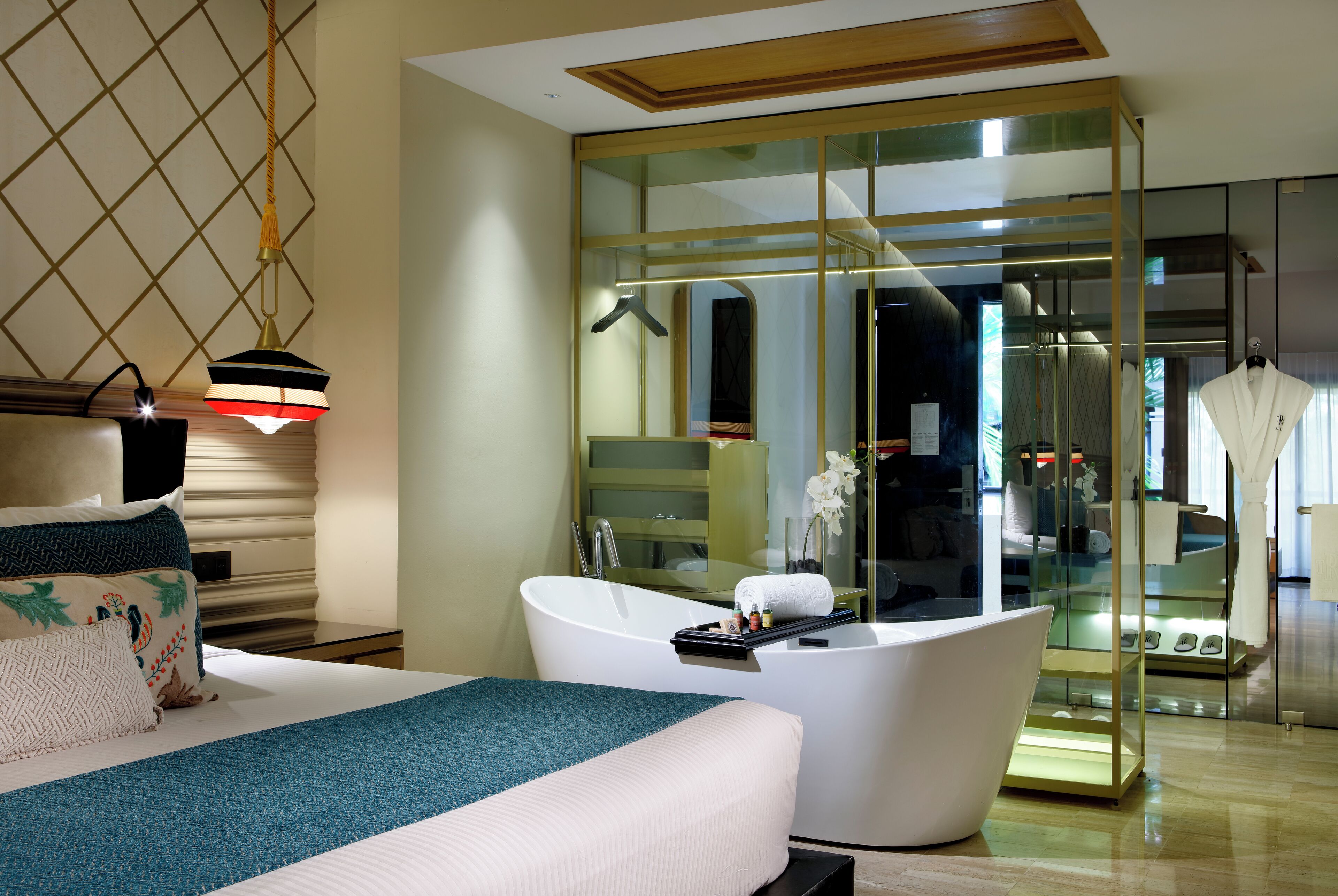 Ein modernes Hotelzimmer mit einem großen Bett, einer freistehenden Badewanne und einem gläsernen begehbaren Kleiderschrank.