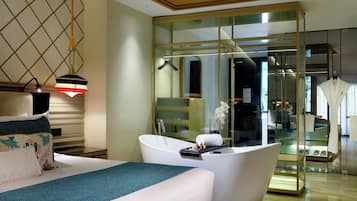 Ein modernes Hotelzimmer mit einem großen Bett, einer freistehenden Badewanne und einem gläsernen begehbaren Kleiderschrank.