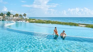 A clear blue pool with a curved edge, surrounded by a tropical landscape and a view of the ocean. - TRS Yucatan Hotel - Adults Only - All Inclusive (Kantenah)