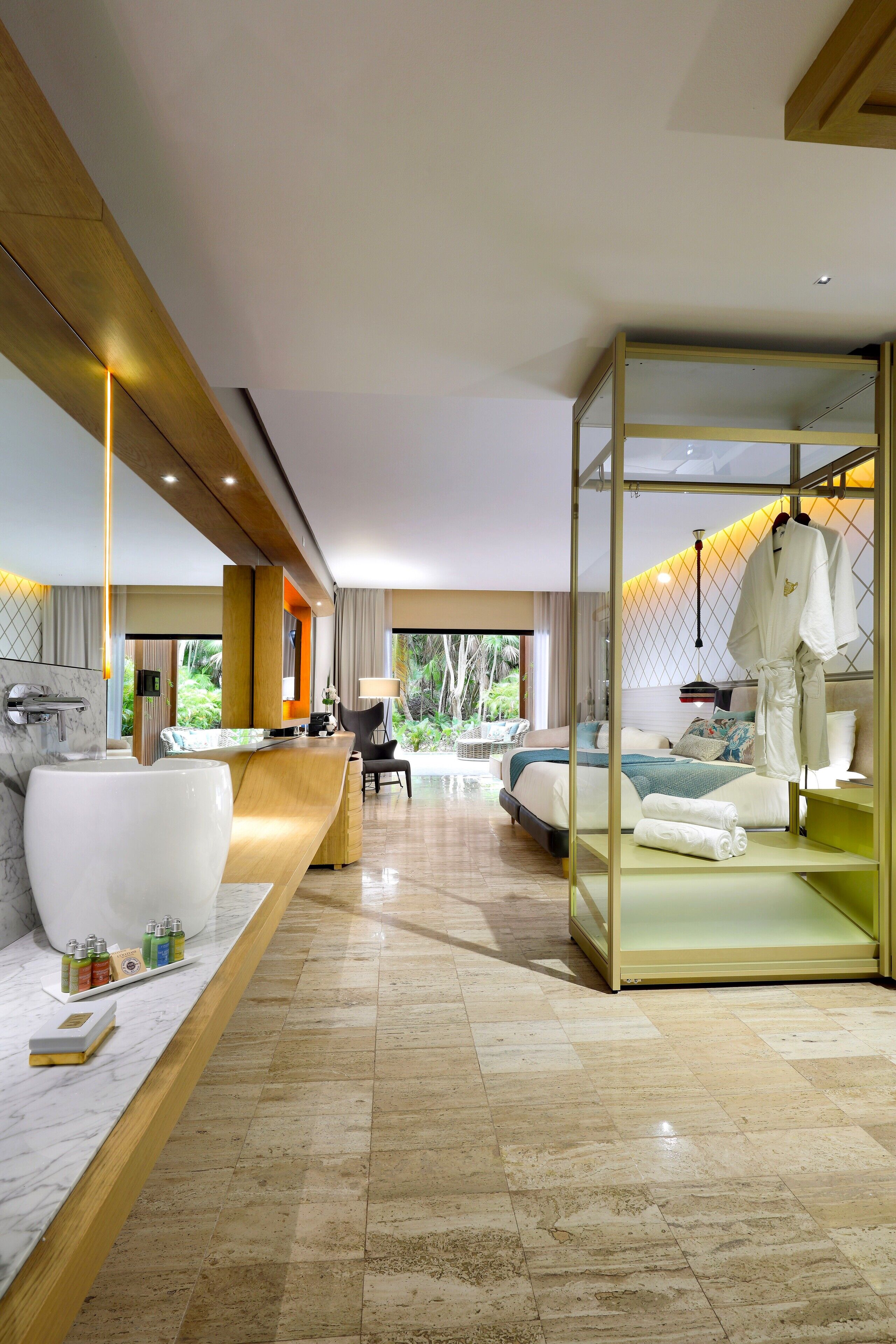Una habitación de hotel moderna con baño de mármol, zona de estar con vistas y un área separada para bata y toallas.