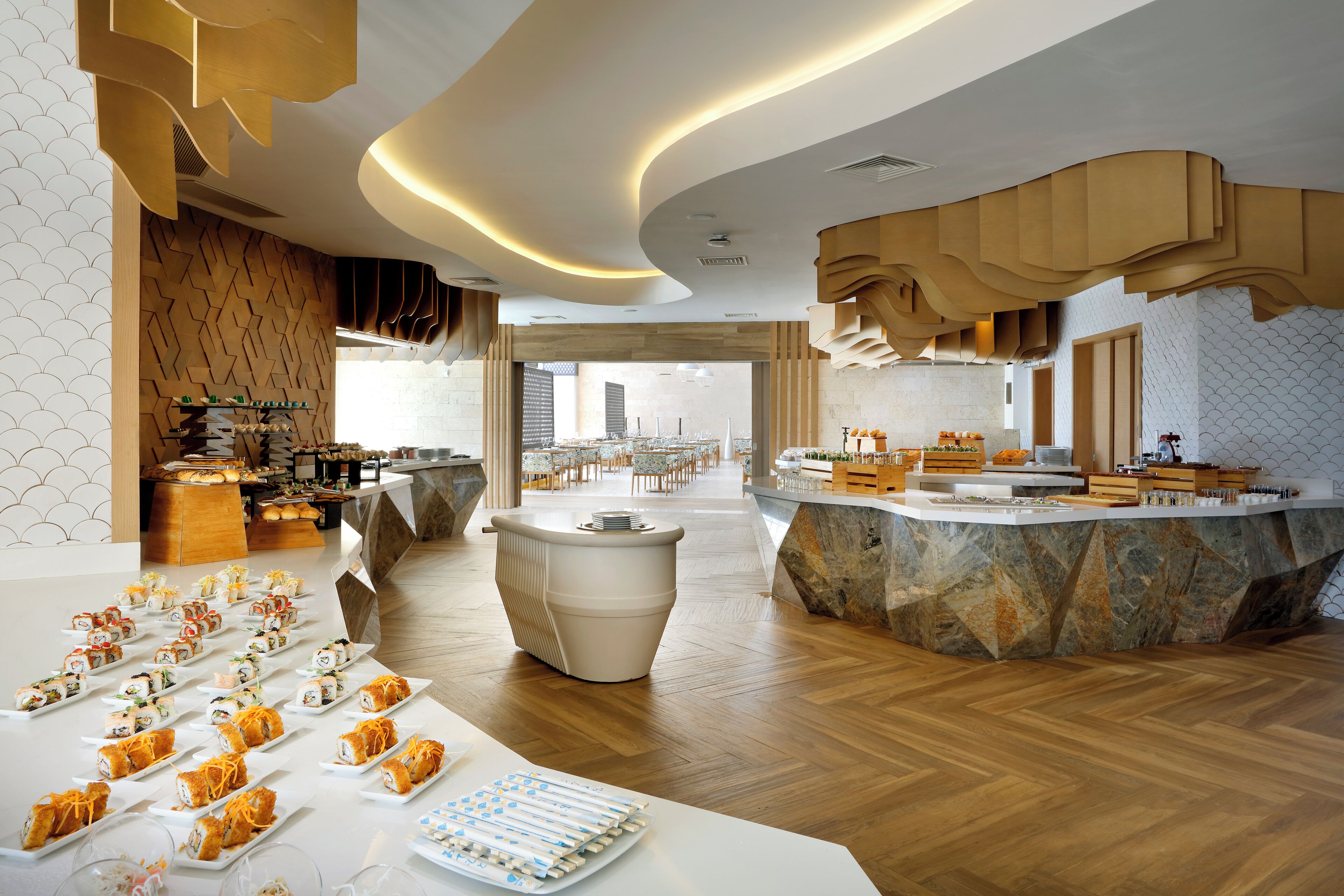 Una hall d'albergo moderna con una reception centrale, un'area buffet e un angolo salotto con tavoli e sedie.