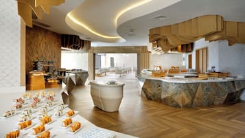 Una hall d'albergo moderna con una reception centrale, un'area buffet e un angolo salotto con tavoli e sedie.