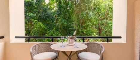A balcony with two wicker chairs and a small round table, overlooking a lush green garden.