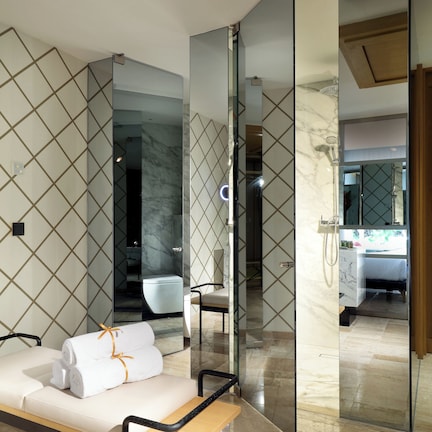 A modern bathroom with a glass-enclosed shower, a bench with towels, and a marble floor.