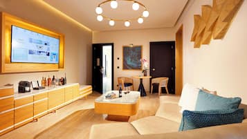 A modern hotel lobby with a large digital display, a wooden reception desk, a round coffee table, and a seating area with a sofa and chairs.