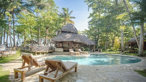 A pool area with lounge chairs and a thatched-roof hut.
