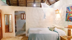 A bedroom with a bed, a nightstand, a mirror, a door, and a wall-mounted light fixture.