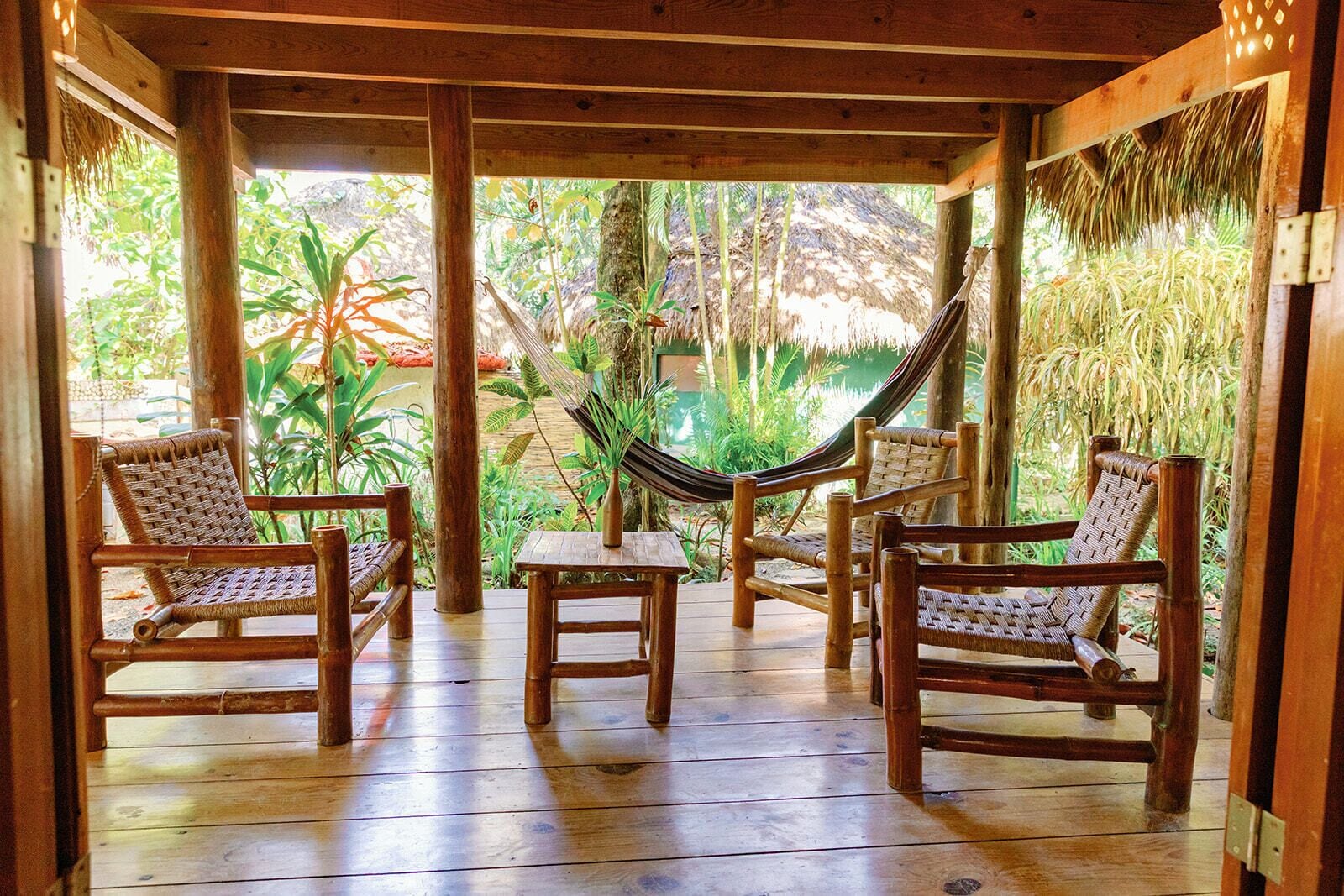 Una terraza de madera con cuatro sillas de mimbre y una hamaca.