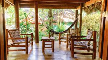 Una terraza de madera con cuatro sillas de mimbre y una hamaca.