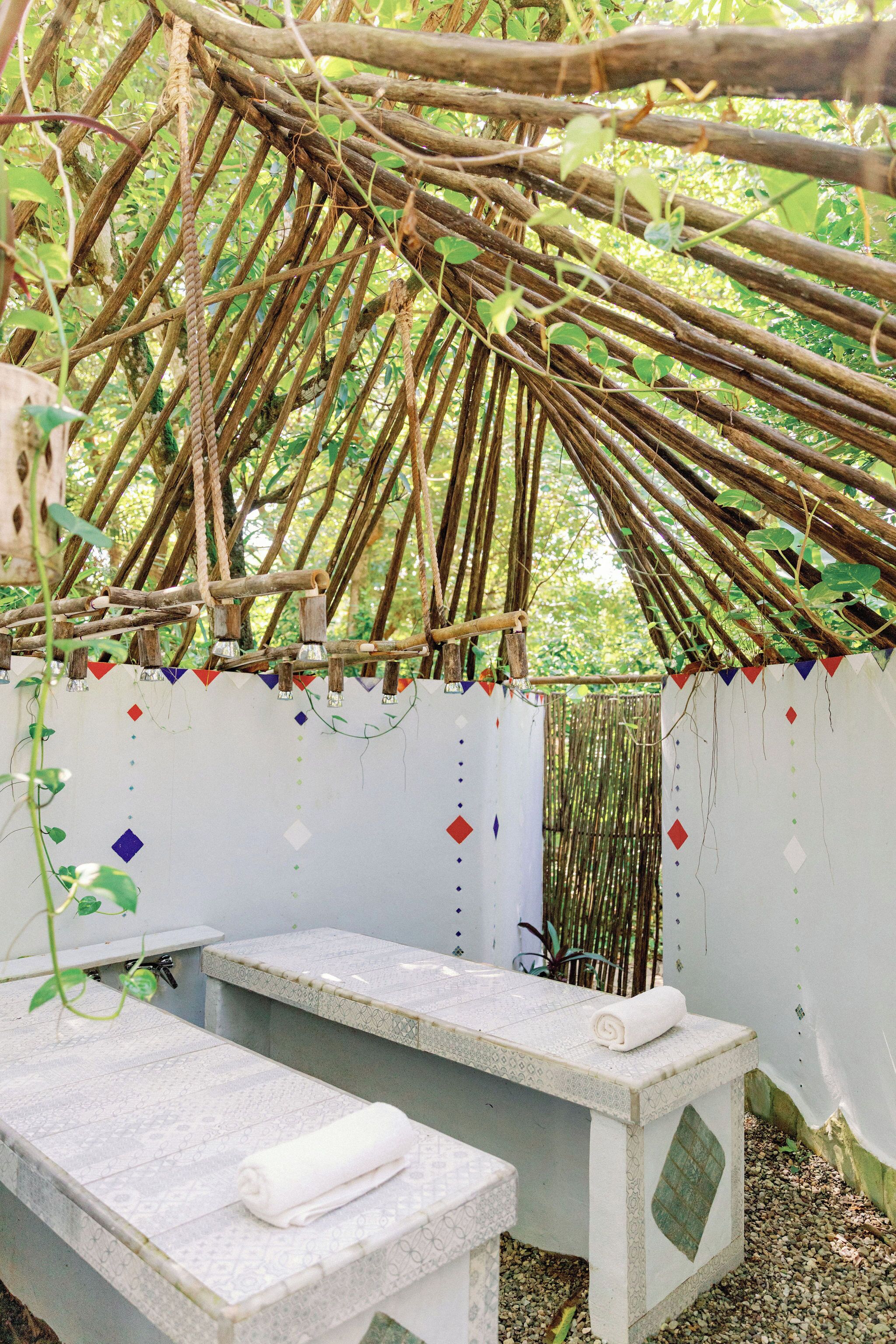 A rustic outdoor seating area with a thatched roof, benches, and a decorative wall.