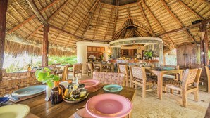 A restaurant with a thatched roof and wooden furniture, featuring a central dining area with a curved counter and a kitchen visible through an open wall. - Natura Cabana Boutique Hotel & Spa (Cabarete)