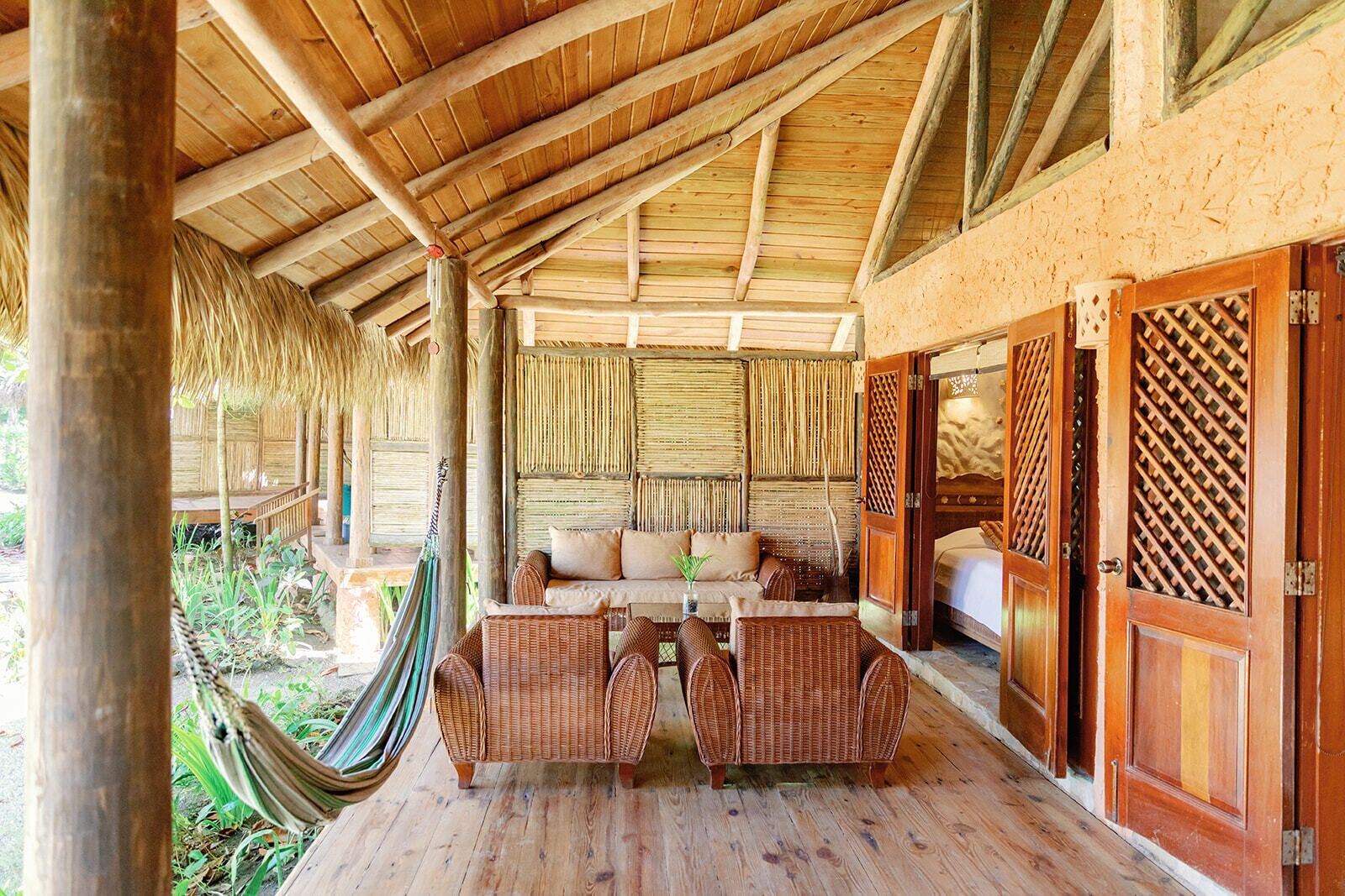 A covered outdoor seating area with wicker furniture, a hammock, and a bamboo wall.