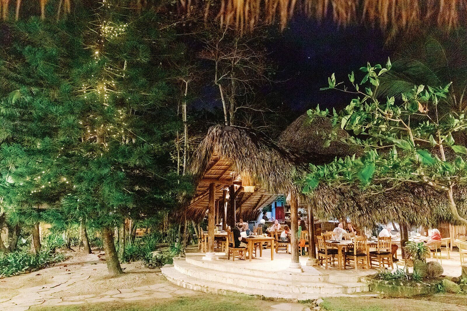 Un espacio de comedor al aire libre con estructuras de techo de paja y mesas y sillas de madera.
