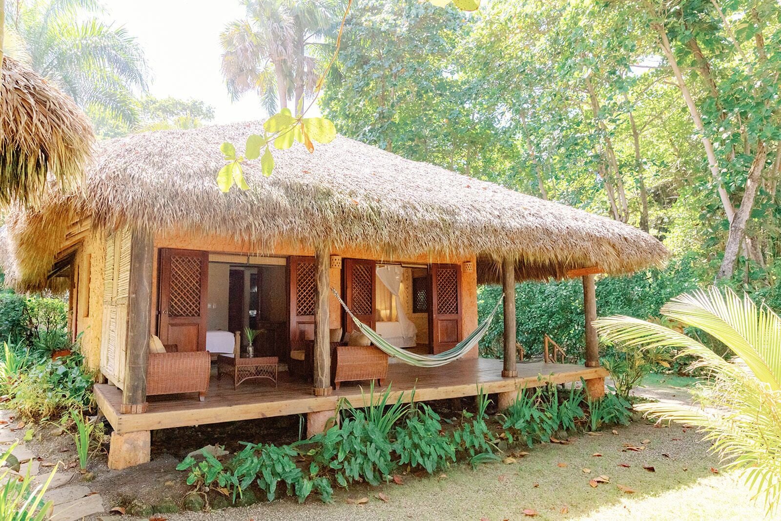 A thatched-roof hut with a porch, wooden furniture, and a hammock.