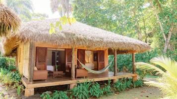 Uma cabana com telhado de palha, varanda, móveis de madeira e uma rede.