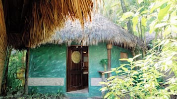 A thatched-roof hut with a green exterior, a wooden door, and a small window.