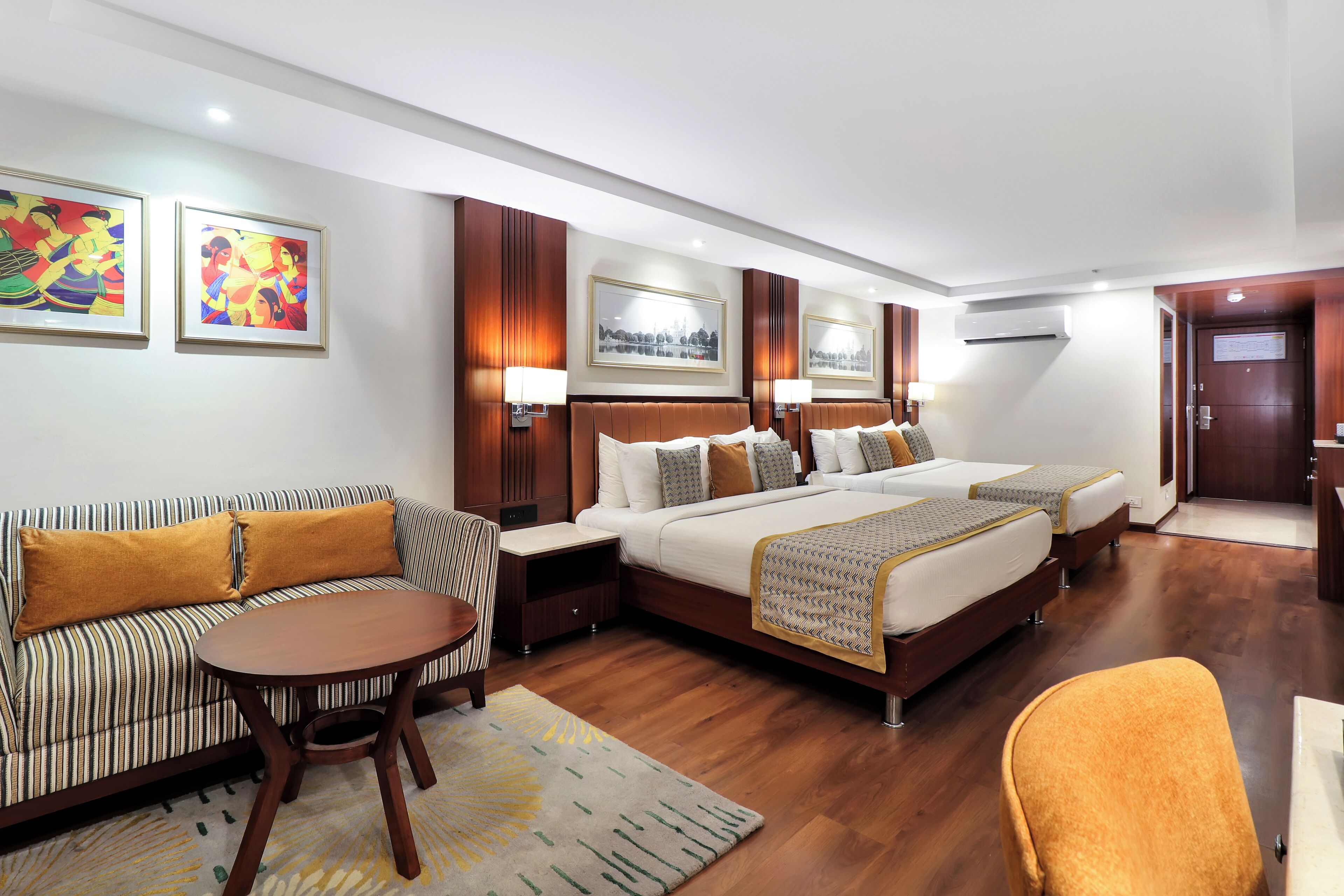 Una camera d'hotel con un divano, due letti, un tavolo rotondo e opere d'arte alle pareti.