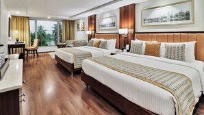 A hotel room with two beds, a desk, a chair, and large windows with a view of palm trees. - Fortune Park Panchwati, Kolkata - Member ITC Hotels' Group (Howrah)
