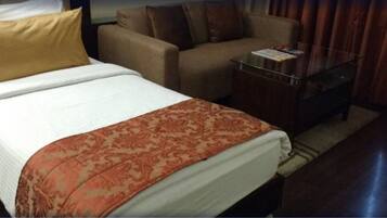 A hotel room with a bed, a sofa, a glass coffee table, and a small table with a magazine.