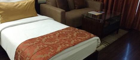 A hotel room with a bed, a sofa, a glass coffee table, and a small table with a magazine.