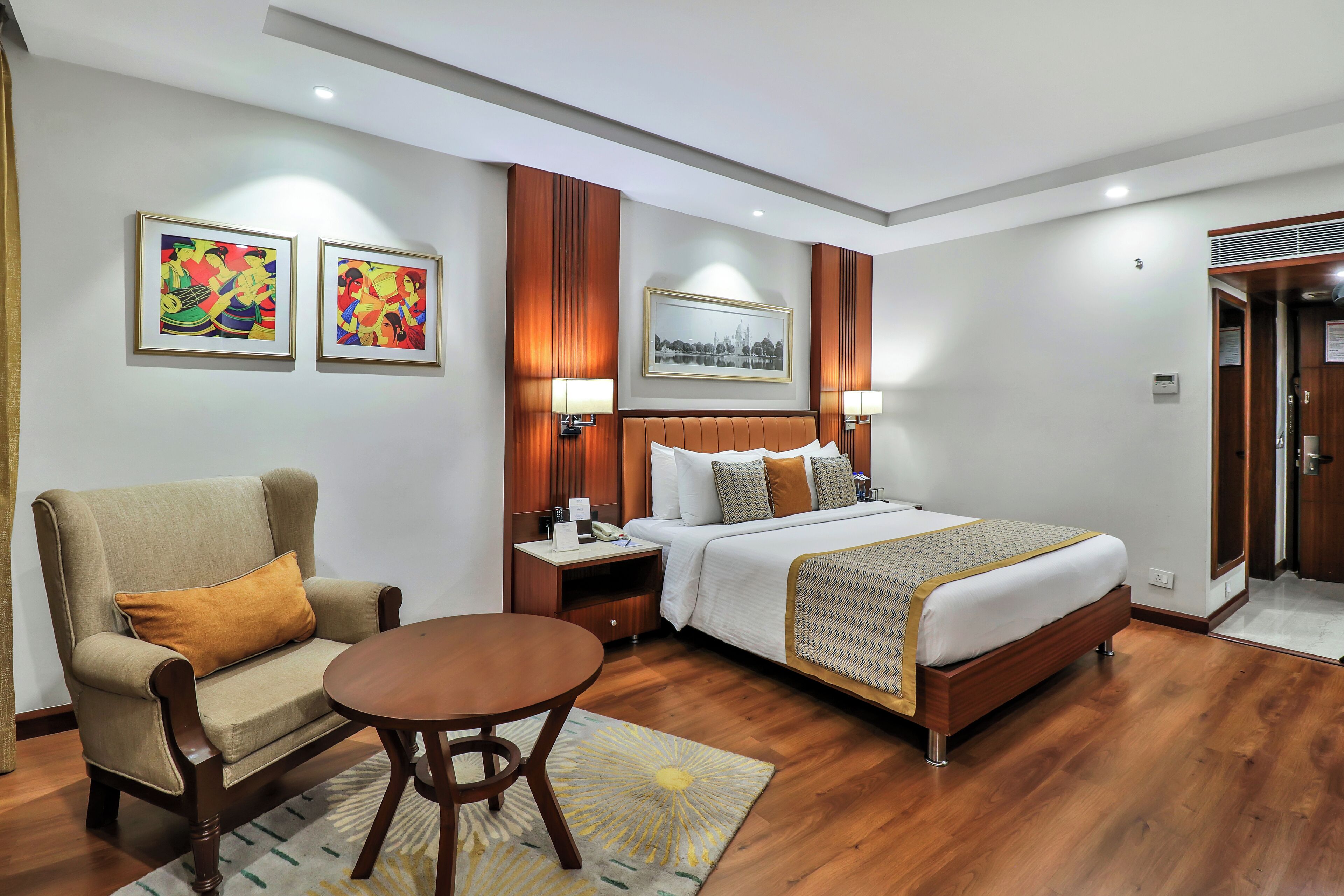 A hotel room with a bed, a chair, a table, and artwork on the walls.
