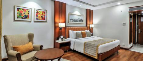 A hotel room with a bed, a chair, a table, and artwork on the walls.