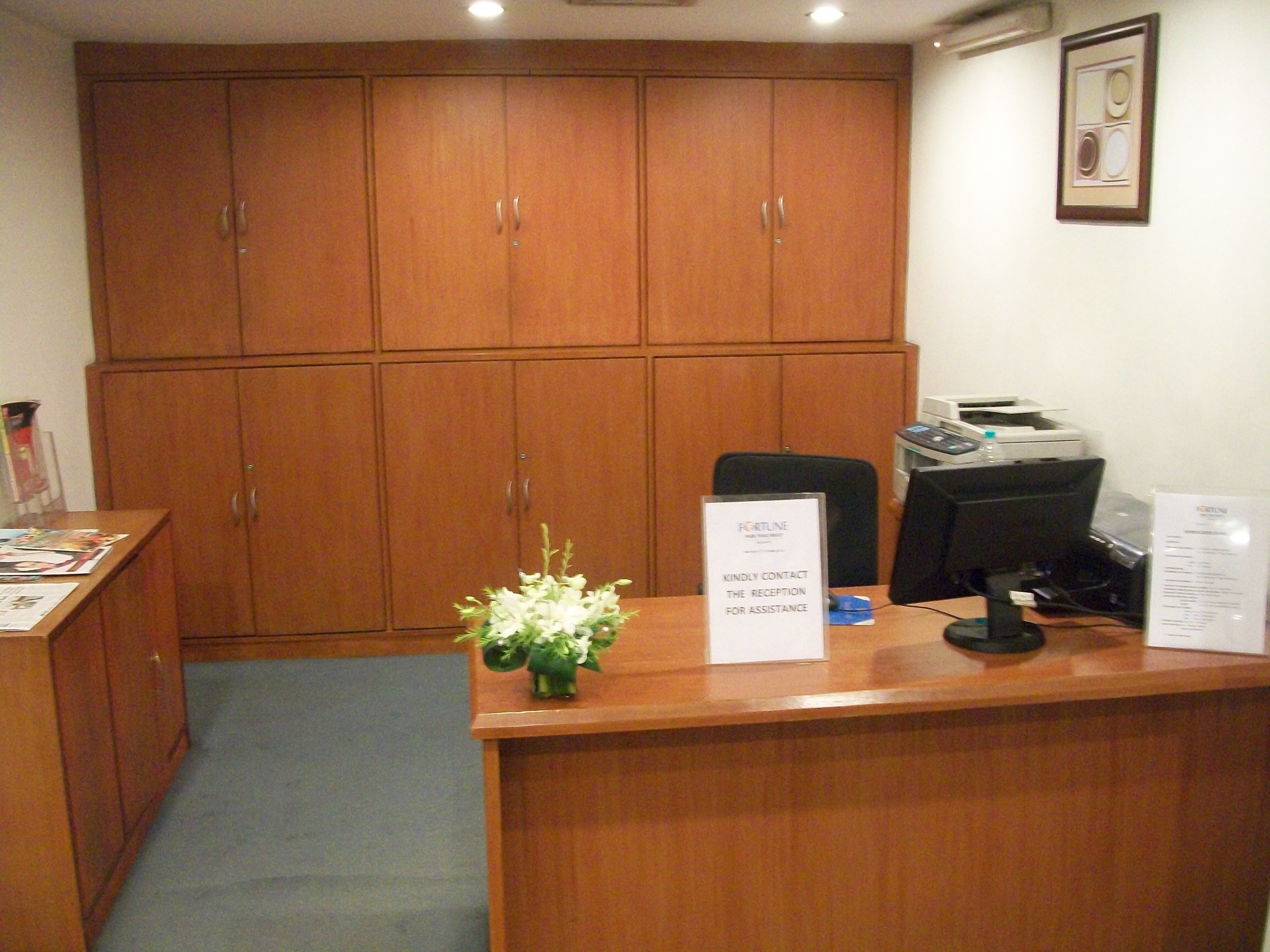 Una recepción con un cartel, una computadora e impresora. Se observan armarios de madera al fondo.