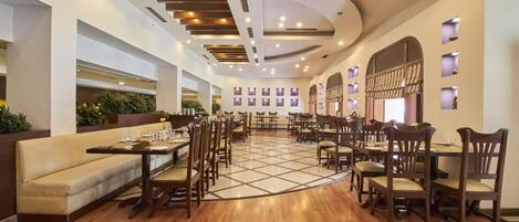 A spacious restaurant with wooden flooring, multiple dining tables and chairs, and recessed lighting on the ceiling.