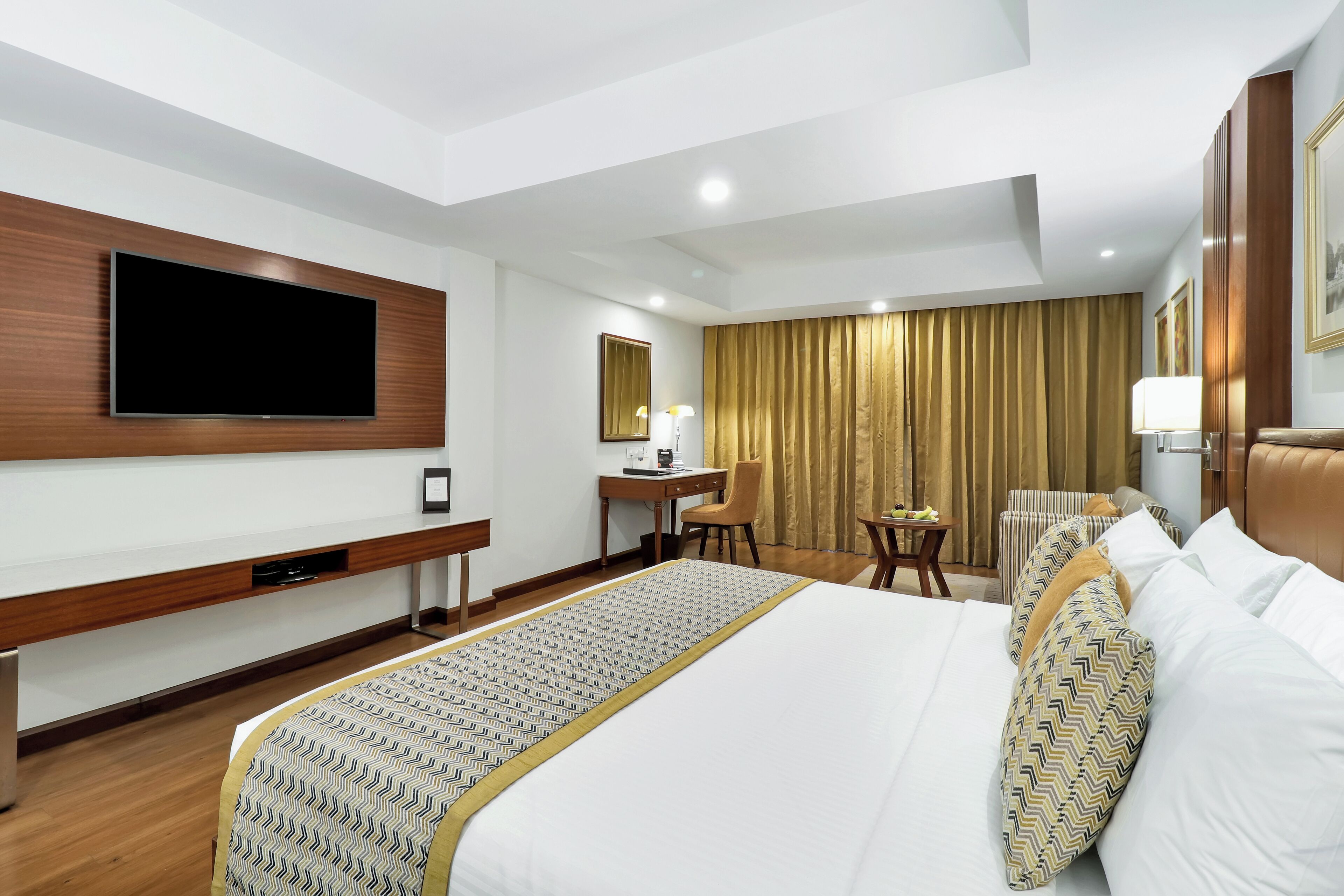 Habitación de hotel con una cama grande, un escritorio, una silla, un televisor montado en la pared y una ventana con cortinas.