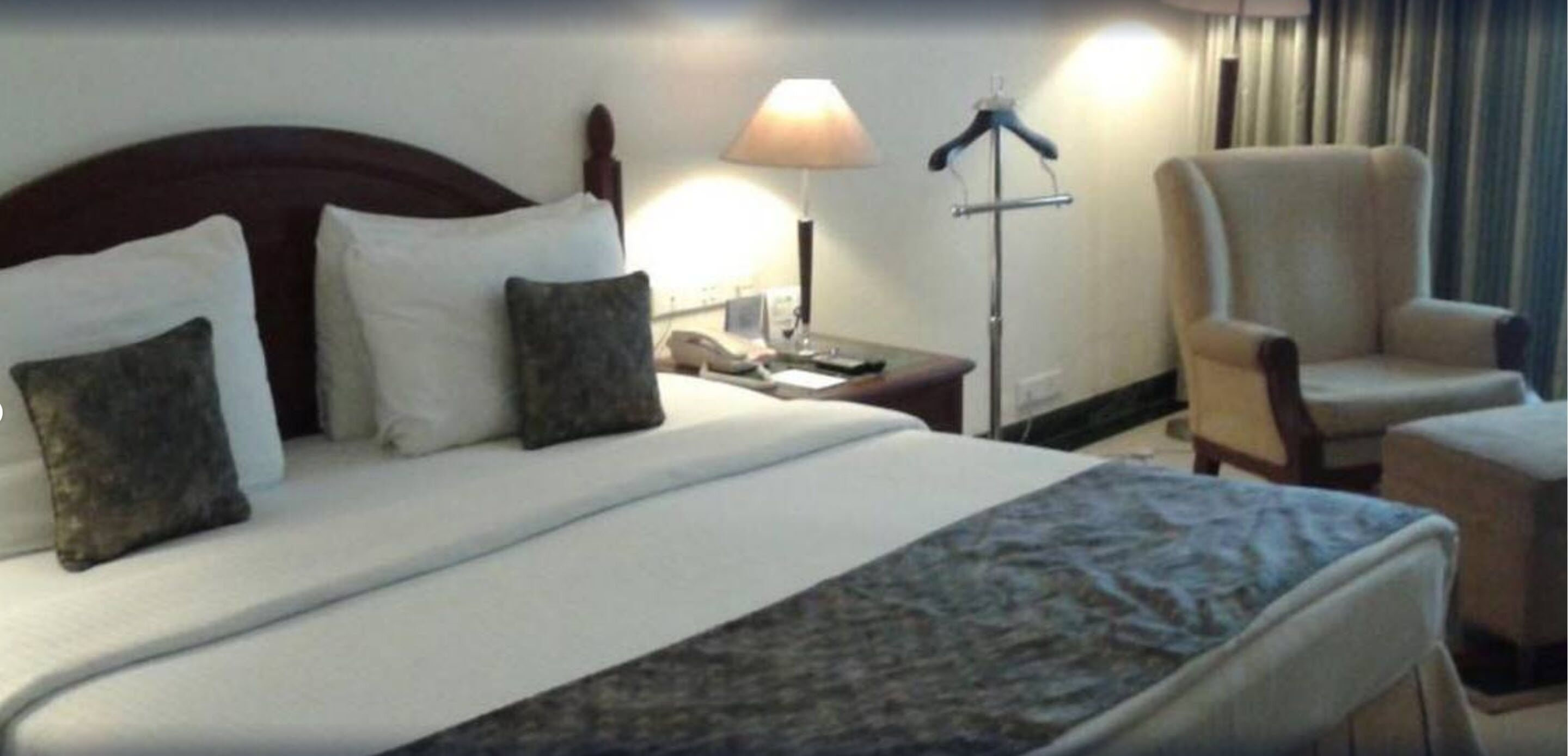 A hotel room with a bed, a nightstand, a lamp, a chair, and a desk.