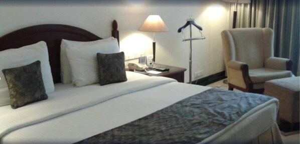 A hotel room with a bed, a nightstand, a lamp, a chair, and a desk.