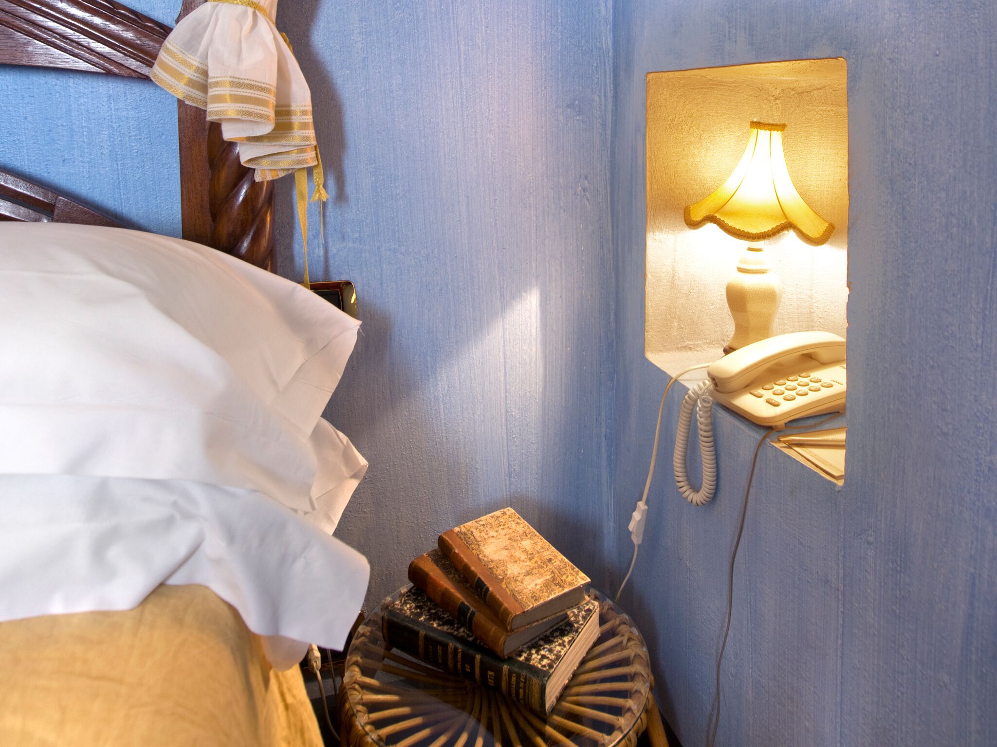 A hotel room with a bed, a bedside lamp, a telephone, and a small table with books.