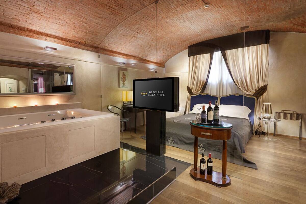 Een moderne hotelkamer met een ruime badkuip, een televisie, een bed met gordijnen en een klein tafeltje met flessen.