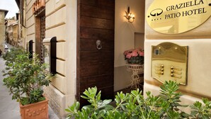 A hotel entrance with a wooden door, a potted plant, a wall-mounted light fixture, and a brass doorbell. - Graziella Patio Hotel (Arezzo)