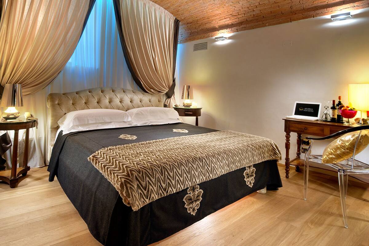 Een slaapkamer met een gestoffeerd hoofdeinde, een groot bed met een bedovertrek met patroon, een bureau met een laptop en een stoel.