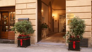 A hotel entrance with a stone facade, a sign for room number 23, and two potted plants with red ribbons. - Graziella Patio Hotel (Arezzo)
