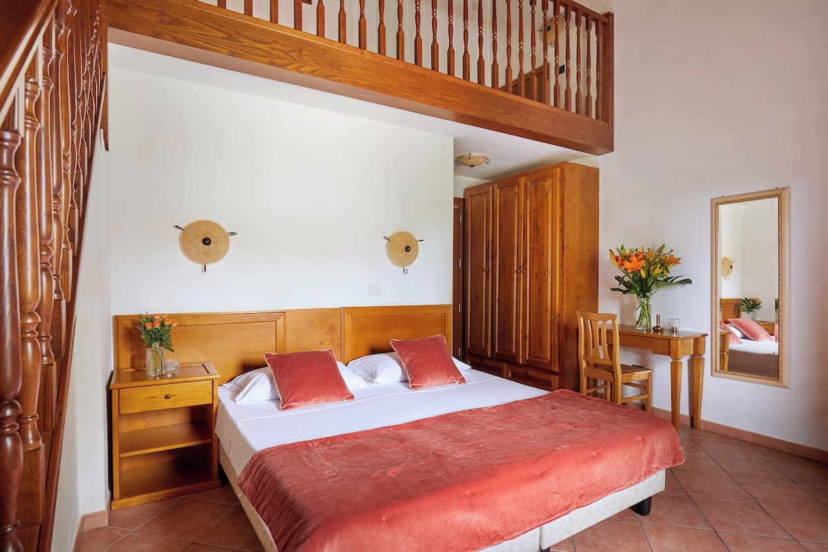 A bedroom with a large bed, wooden headboard, bedside tables, a desk, and a mirror.