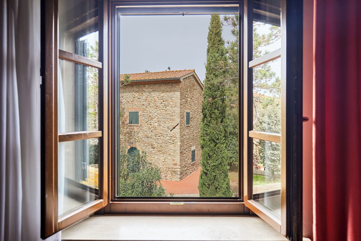 A stone building with a tiled roof, viewed through an open window with wooden frames.