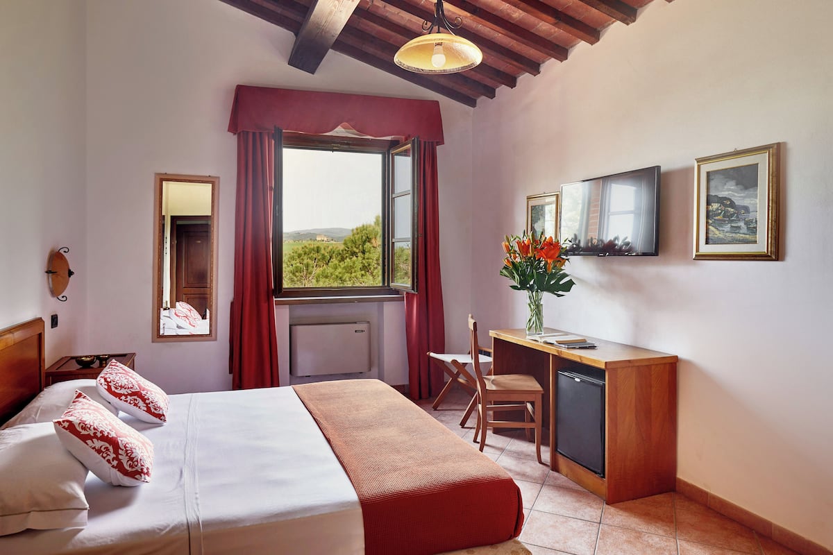 A hotel room with a bed, a desk, a chair, a small refrigerator, and a window with a view.