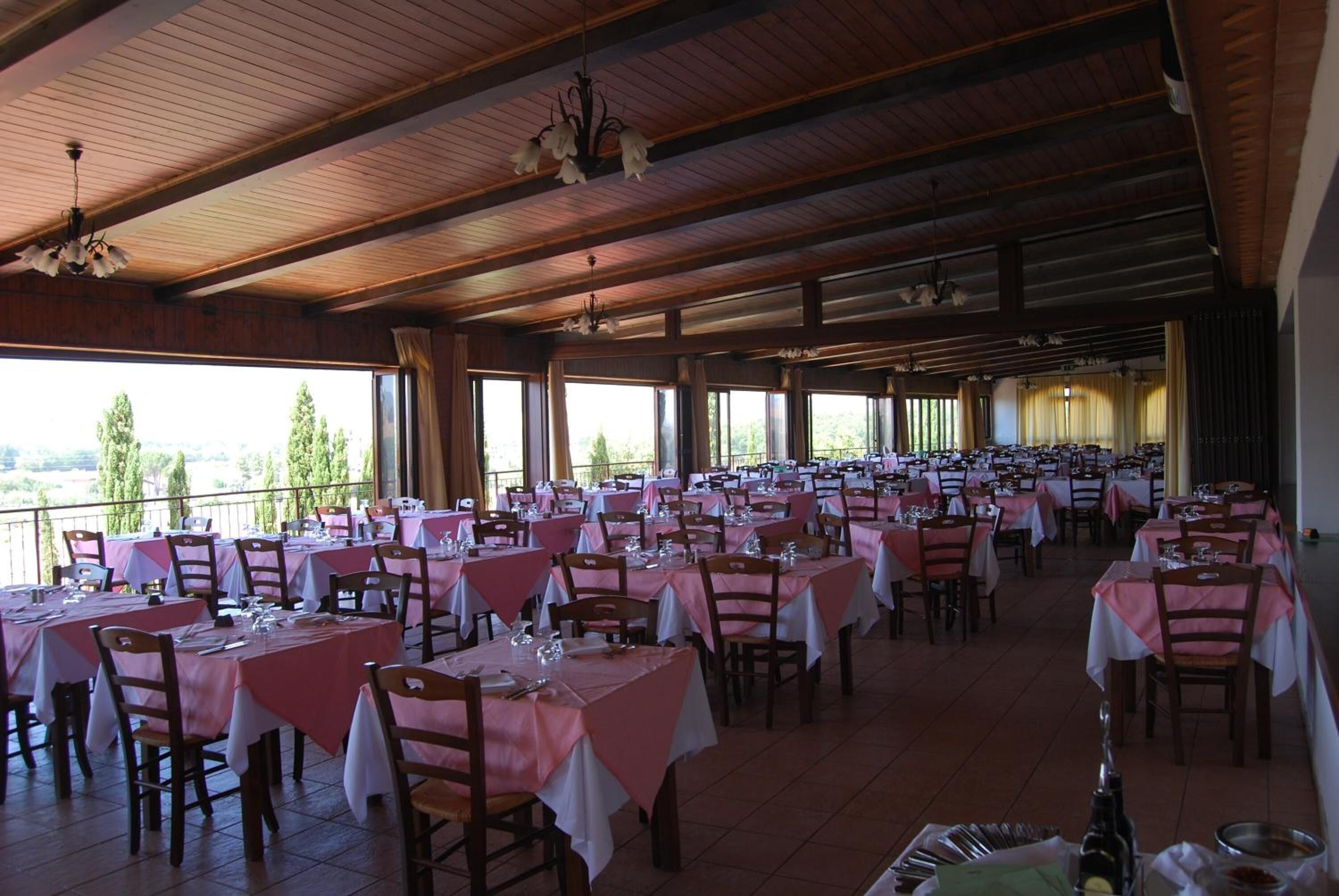 Un vaste espace dédié à la salle à manger, avec de nombreuses tables et chaises, de grandes fenêtres offrant une vue sur l’extérieur et un plafond en bois agrémenté de luminaires suspendus.