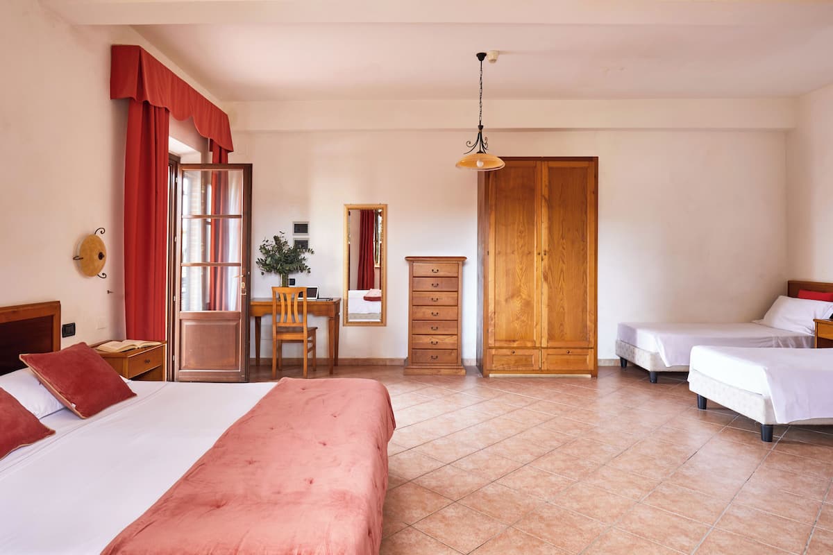 A hotel room with two beds, a desk with a chair, a wooden wardrobe, and a large mirror.