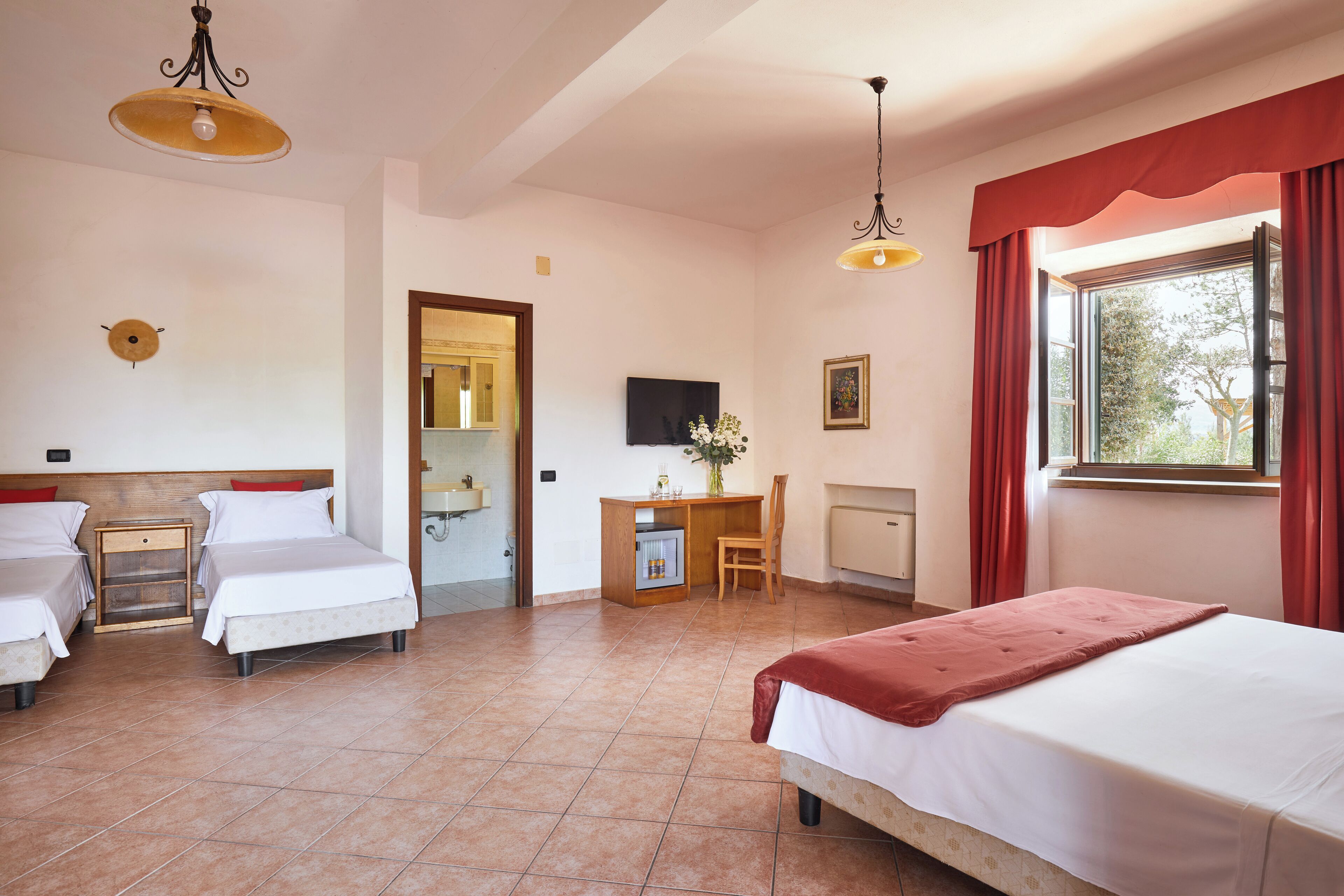 Habitación de hotel con dos camas, un escritorio, una silla, un televisor y una ventana con cortinas rojas.