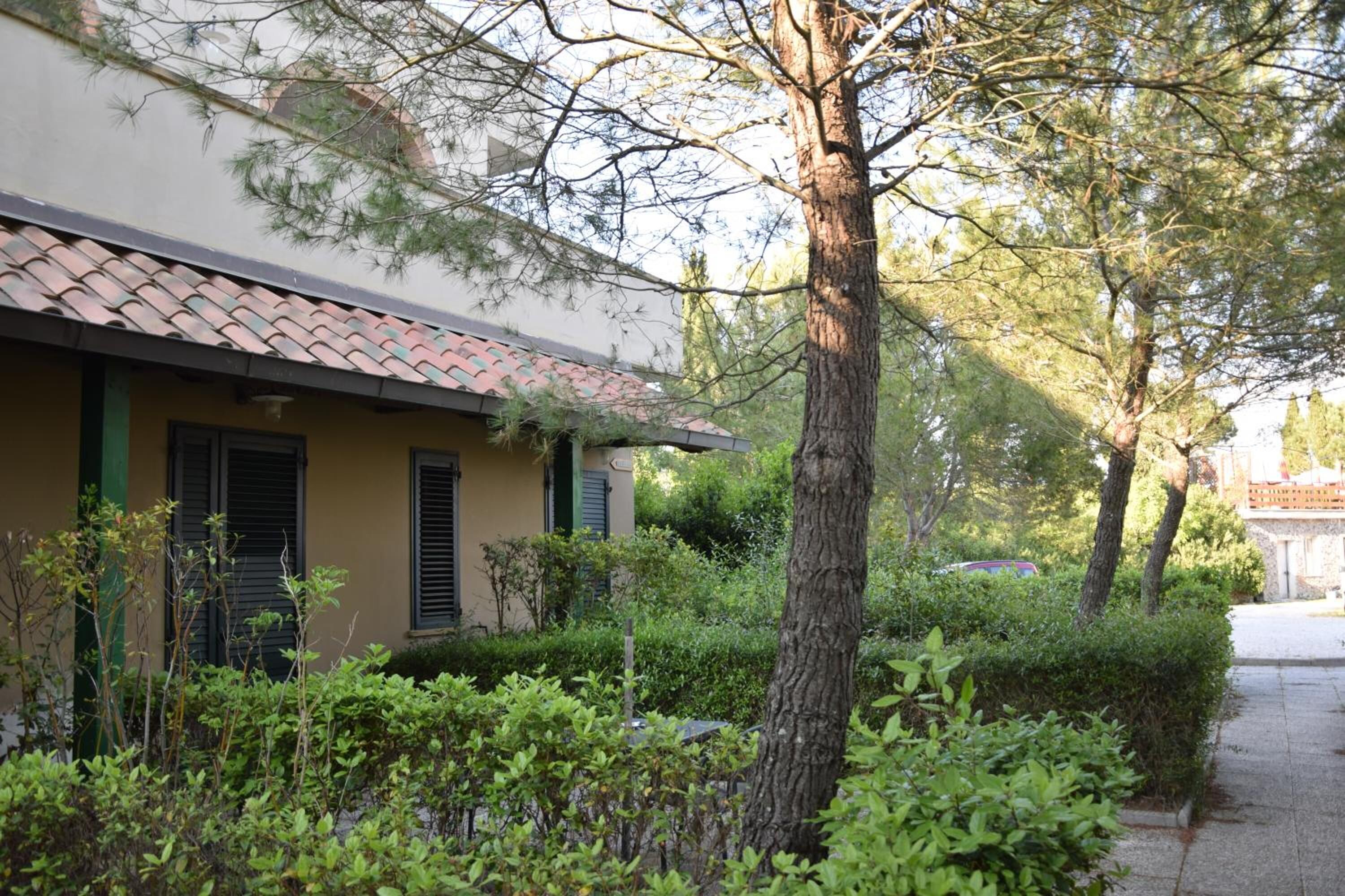 A building with a tiled roof and green shutters, surrounded by lush greenery and trees.