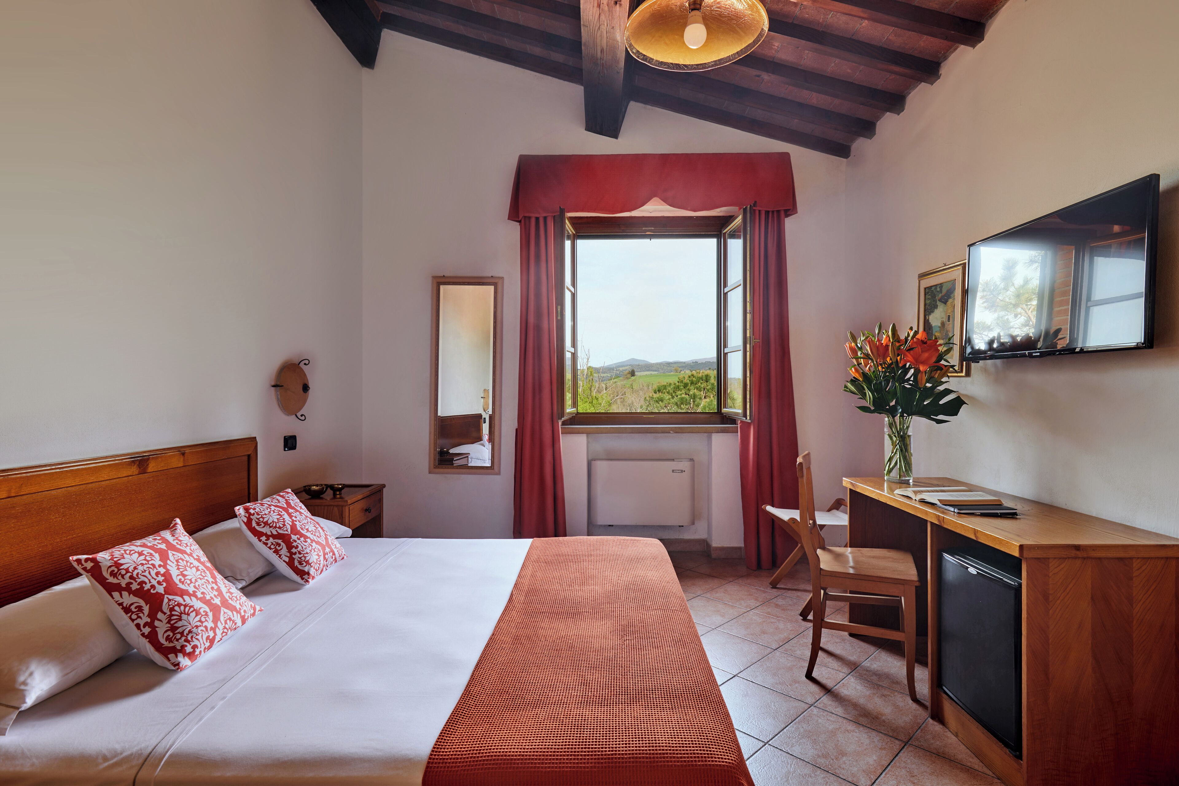 A hotel room with a bed, a desk, a chair, a TV, and a window with a view of the countryside.