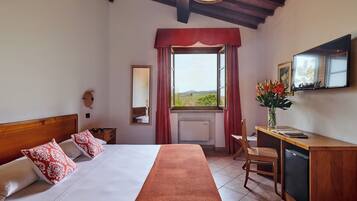 Habitación de hotel con cama, escritorio, silla, televisor y ventana con vista al campo.