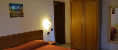 A bedroom with a bed, a wardrobe, a nightstand, a wall-mounted lamp, and a painting.