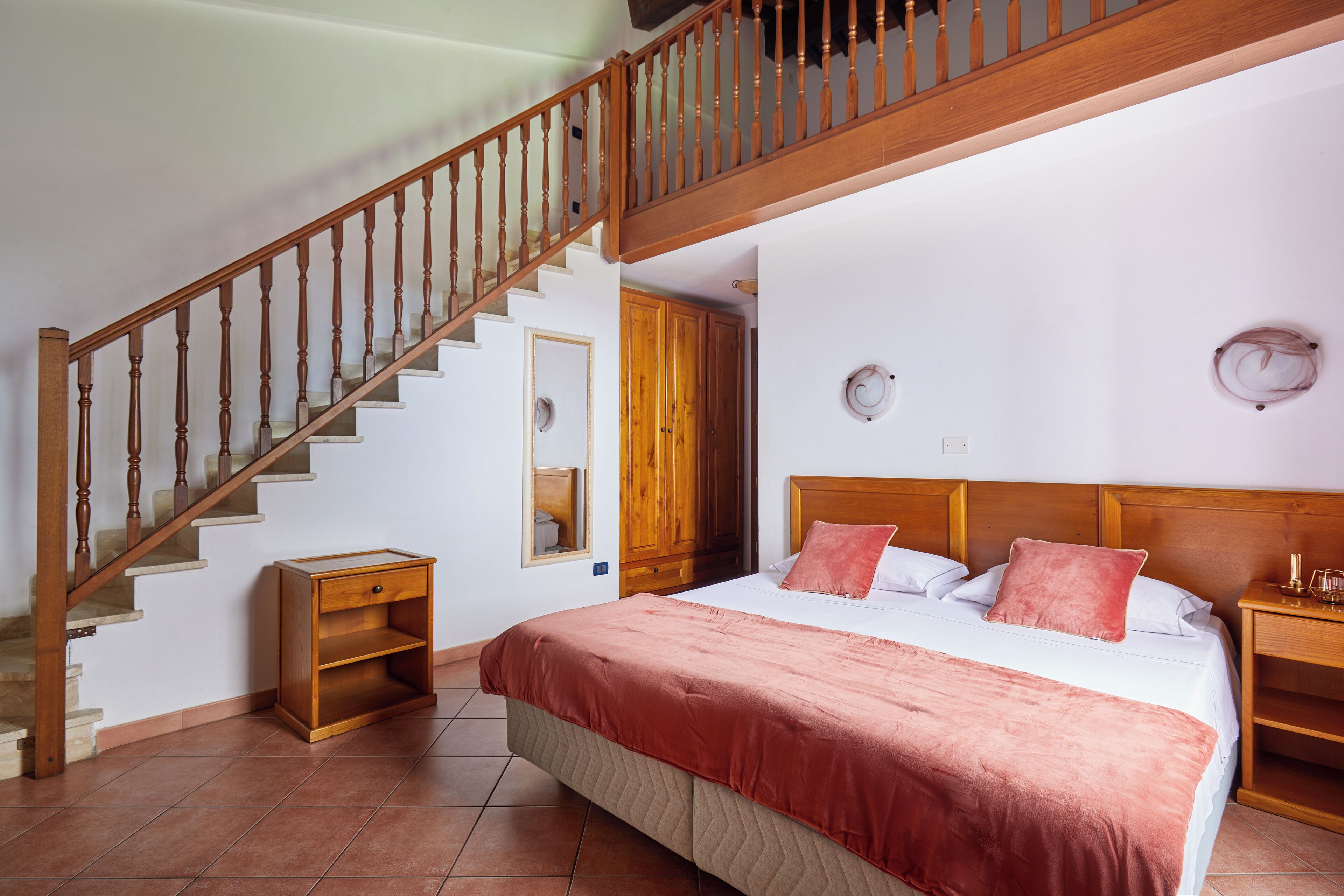 A bedroom with a wooden staircase, a bed with a pink blanket, a nightstand, and a wooden wardrobe.