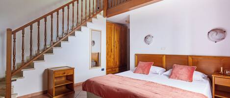 A bedroom with a wooden staircase, a bed with a pink blanket, a nightstand, and a wooden wardrobe.
