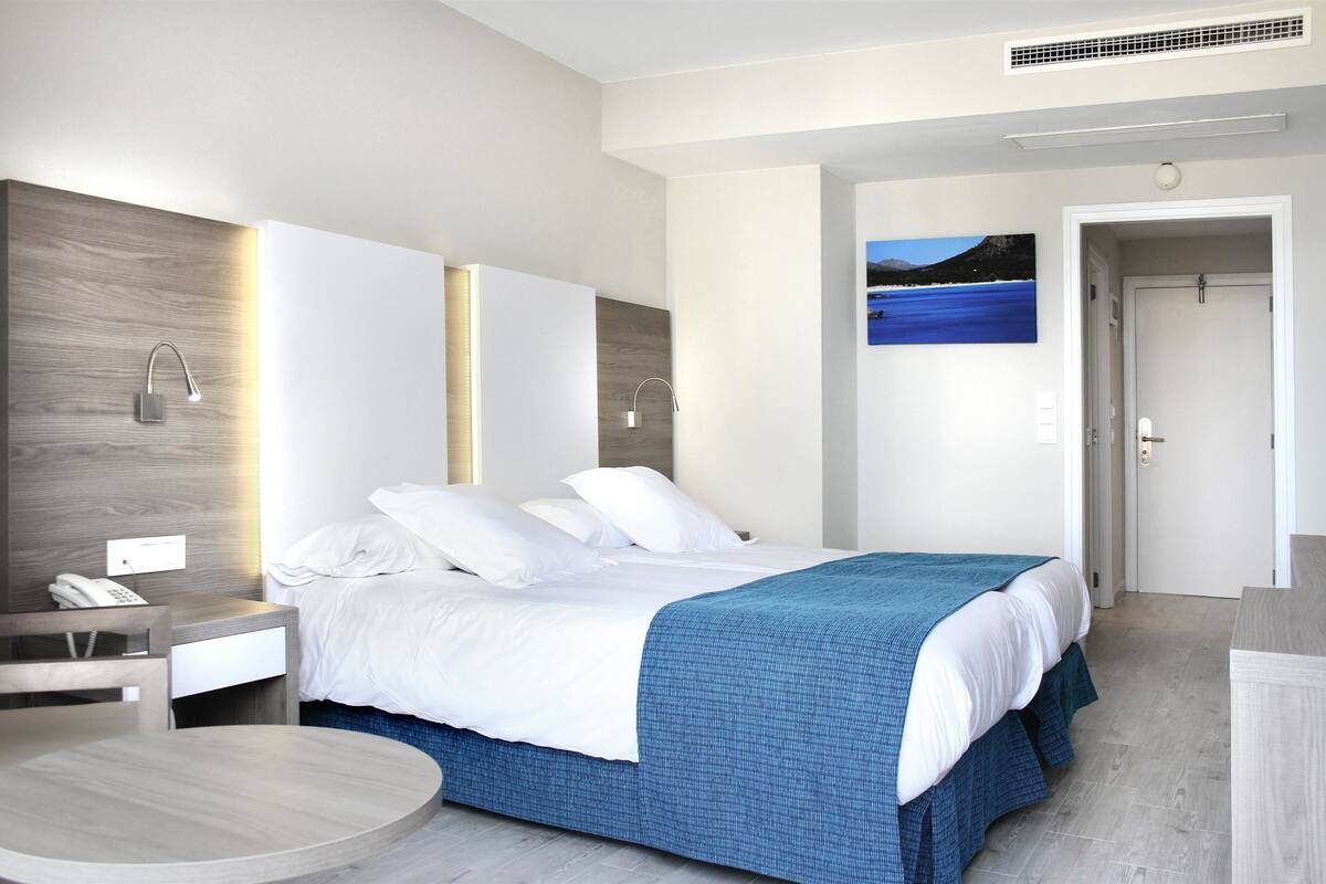 Une chambre d’hôtel moderne avec un grand lit, des tables de chevet, une table ronde et un tableau au mur.